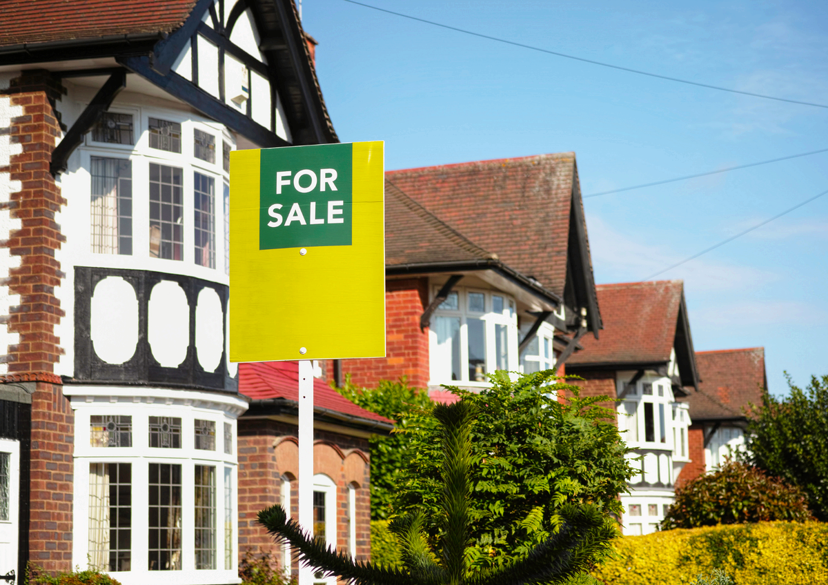 A traditional house with a for sale sign outside